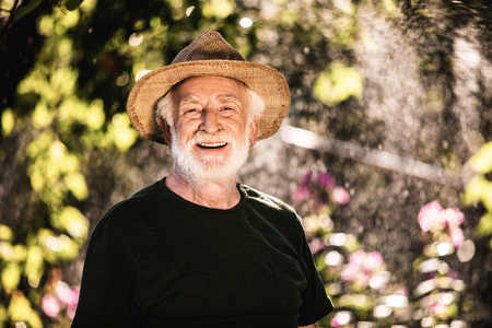 Smiling senior man in straw hat standing against a blooming gardenの写真素材