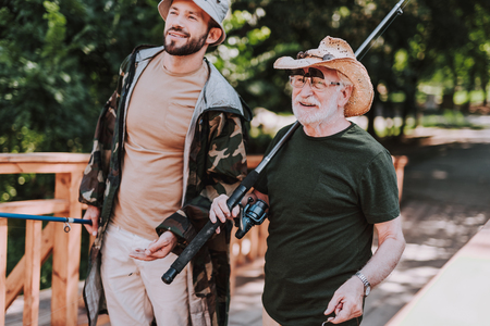Waist up of a cheerful aged man holding fishing equipment while spending time with his sonの写真素材