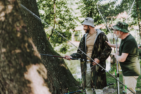 Cheerful young bearded man holding a rod while fishing with his fatherの写真素材