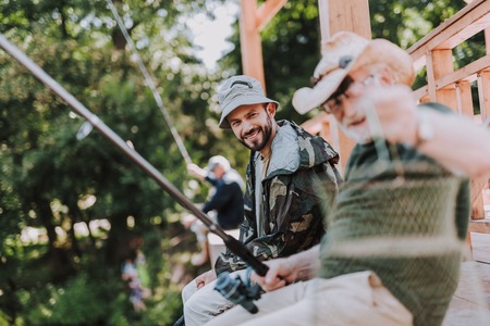 Cheerful bearded man fishing with his father while spending weekend with pleasureの写真素材