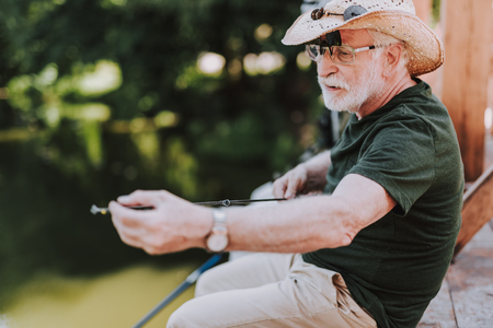 Nice elderly bearded angler holding a rod while fishing on the weekendの写真素材