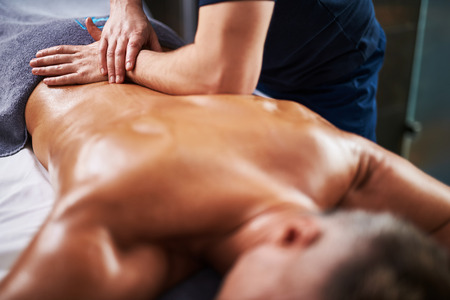 Close up of masseur hands doing therapeutic massage for male client while he lying on massage tableの写真素材