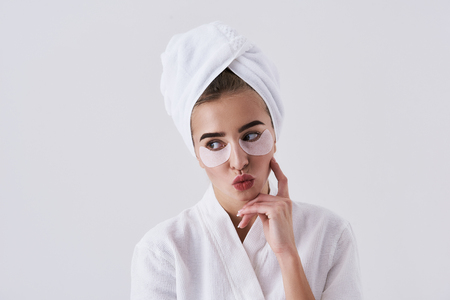Portrait of beautiful girl with masks on lower eyelids making cute grimace while resting chin on hand. Isolated on white backgroundの写真素材