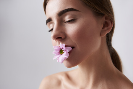 Close up portrait of charming girl with flower closing eyes with pleasure. Isolated on white backgroundの写真素材