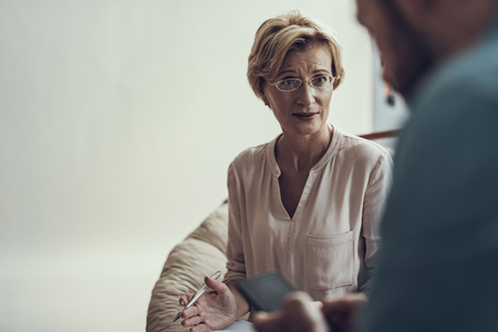 Emotional middle aged psychotherapist gesturing and frowning while feeling worried and looking at her clientの写真素材
