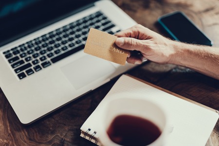 Top view photo of mature man hand holding gold credit card against blurred laptopの写真素材