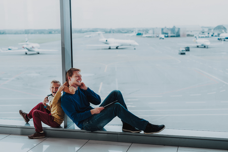 Jolly parent with his child is sitting near large window at airport.の写真素材