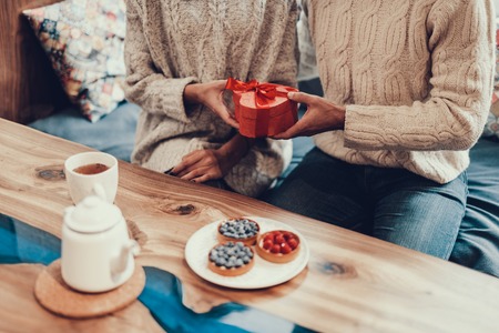 Cropped photo of two people sitting in sweet cafe and holding small box present in hands