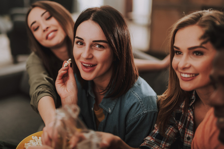 Portrait of beautiful young ladies eating popcorn and smilingの写真素材