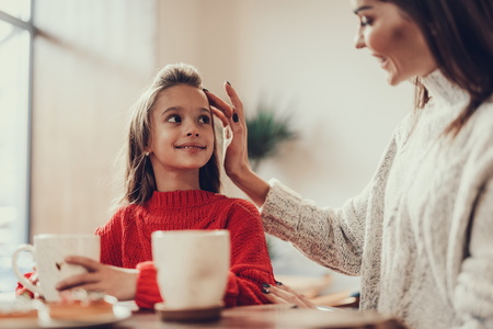 Tender mom sitting in small cafe with her daughter. She touching little girls hair by her fingers and smilingの写真素材