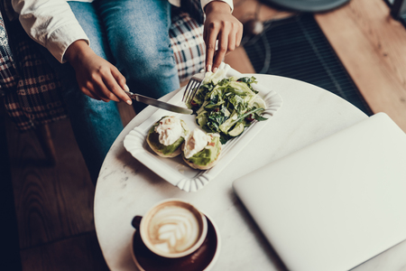 Top view of woman in cafe. She eating breakfast and sitting behind table with notebook and cup of beverageの写真素材