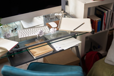 Glass table with computer, spiral notebook, sketchbook, pencil and crumpled paperの写真素材