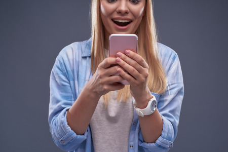 Cropped portrait of pleasantly surprised girl reading message with excellent news on smartphone.の写真素材