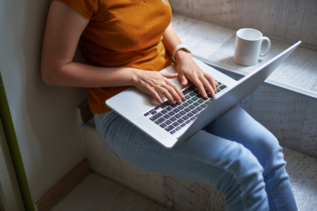 Cropped portrait of busy girl typing on notebook keyboard while sitting on steps with cup of coffeeの写真素材