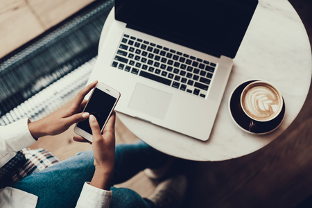 High angle photo of woman in cafe. She holding modern cellular in hands near laptop and cup of coffeeの写真素材