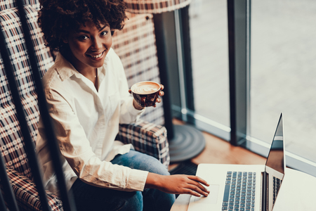 Positive and pretty woman holding cup of beverage and smiling.の写真素材