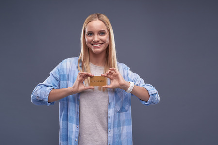 Waist up portrait of charming blond girl holding plastic credit card while looking at camera and smiling.の写真素材