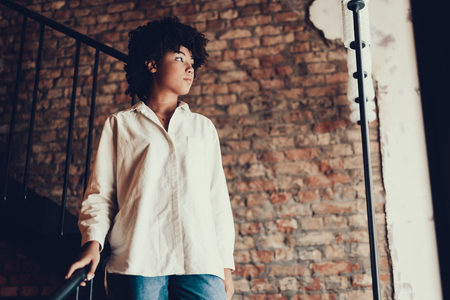 Young woman with calm face looking aside and standing against red brick wall inside cafeの写真素材