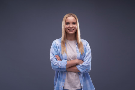 Waist up portrait of cheerful blond girl with crossed arms looking at camera and smilingの写真素材