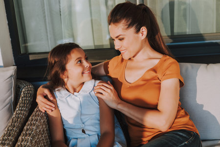 Cheerful caring mother sitting with her pretty daughter while expressing love