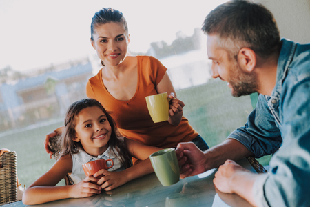 Pleasant nice couple resting with their little daughter at home while drinking teaの写真素材