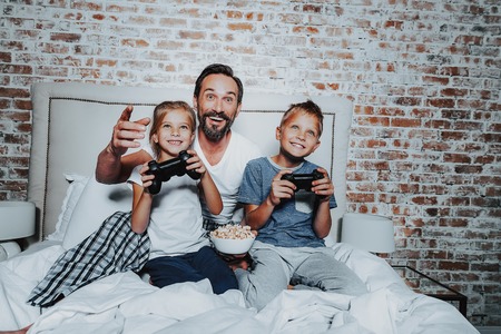 Family relationship concept. Portrait of happy man with popcorn plate watching how his son and...