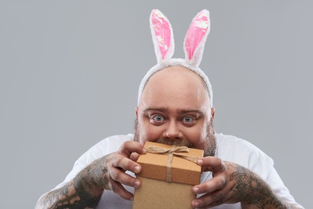 Ready for the party. Funny fat man with tattooed arms standing isolated on the grey background with...