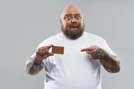 Waist up of happy bearded man standing alone against the grey background and smiling while pointing...