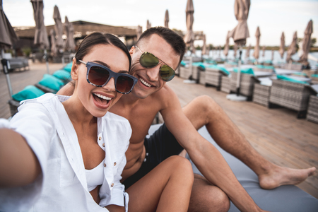 Selfie together. Close up of happy young man and woman smiling and posing for the selfie while relaxing on the beachの写真素材
