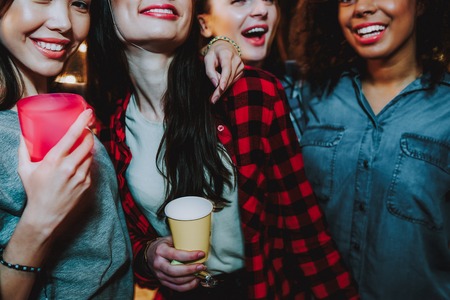 Outgoing young women standing near each other. They are drinking beer, laughing and huggingの写真素材