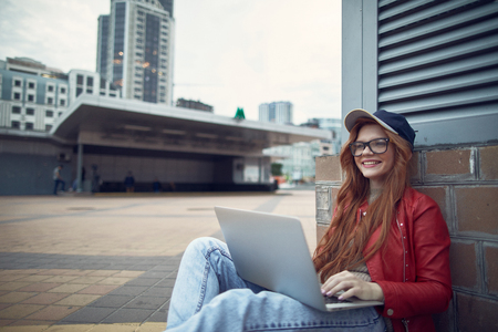 Portrait of beautiful young lady with notebook on her laps looking away and smiling while spending time outdoorsの写真素材