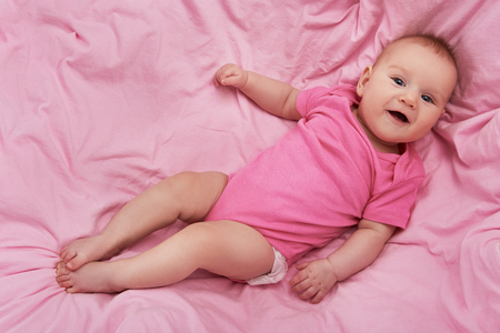 High angle top view photo of cheerful newborn baby looking at camera and lying on pink blanket with smileの写真素材