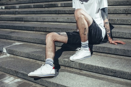 Young man with tattoos on his hands and legs sitting on steps