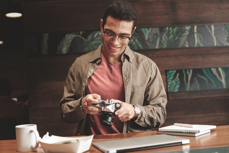Handsome young man in glasses checking retro camera and smiling