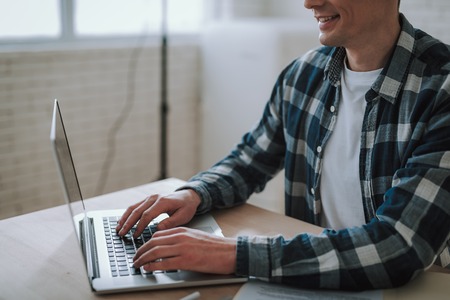 Close up of positive man smiling while typing on his laptop