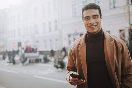 Handsome elegant young man in wireless earphones using cellphoneの写真素材