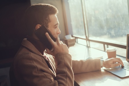 Handsome young man with laptop talking on cellphone