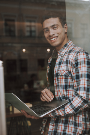 Good-looking young man behind glass using laptopの写真素材