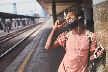 Dancing young man with headphones standing on railway stationの写真素材
