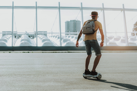 Full length of young man with backpack riding his gyro scooter