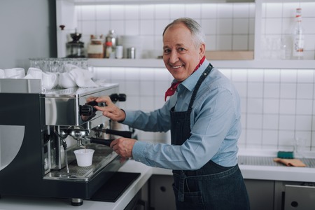 Joyful old man making fresh coffee with professional coffee machineの写真素材