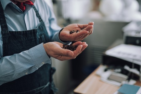 Male hands holding brown roasted coffee beansの写真素材