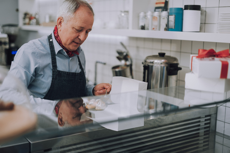 Senior man in apron preparing delicious pastries for special orderの写真素材
