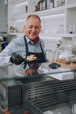 Senior man in black gloves holding delicious cakes in bakery shopの写真素材