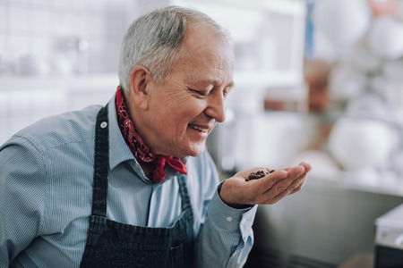 Joyful old man enjoying the aroma of coffee beans in his armsの写真素材