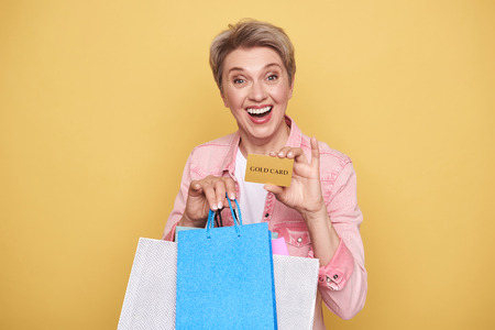 Waist up of happy woman holding colorful shopping bags and gold card