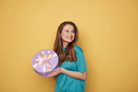 Half length of brunette girl holding a present in arms indoors