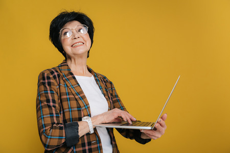 Happy elderly lady wearing fashionable circle eyeglasses and checkered jacket in studio