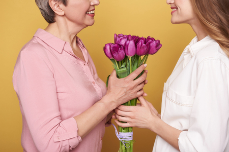 Close up of brown-haired girl giving to her mother flowers for holidayの写真素材