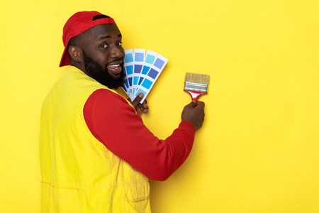 Side view of smiling African man holding paintbrush and palette in armsの写真素材
